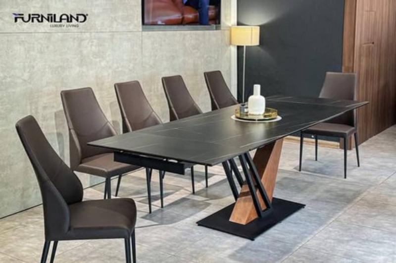 Một bàn tay đang nhẹ nhàng lau chùi bề mặt bàn ghế gỗ phòng khách bằng khăn mềm, thể hiện sự chăm sóc tỉ mỉ, với ánh nắng chiếu qua cửa sổ.