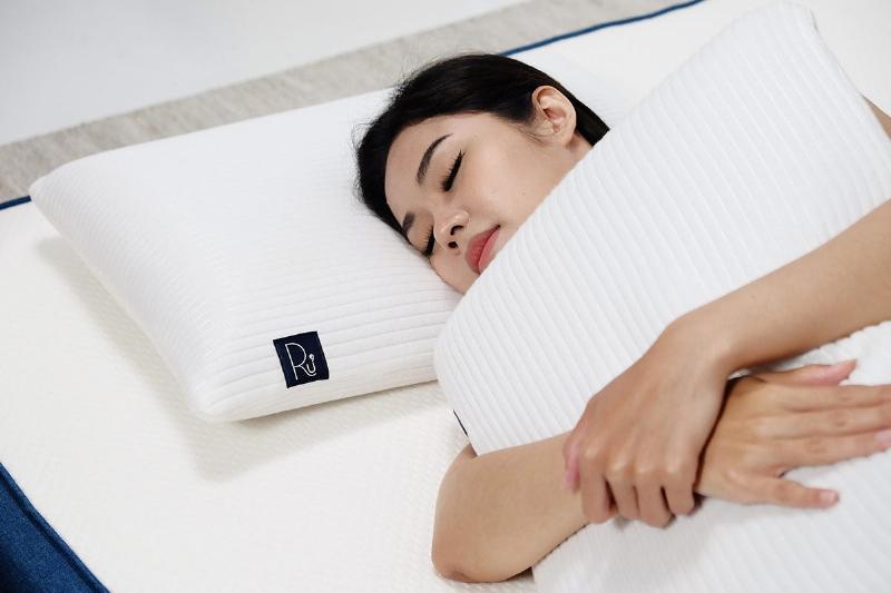 Một chiếc gối cao su non lượn sóng màu trắng trên giường ngủ hiện đại, thể hiện sự thoải mái và nâng đỡ cột sống cổ