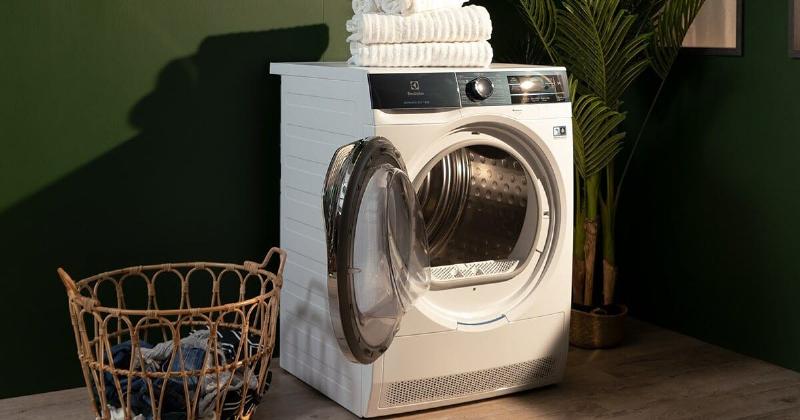 Một chiếc máy giặt đặt trên bộ kê chân chống rung, sàn nhà sạch sẽ và thông thoáng trong một không gian giặt giũ hiện đại, đầy ánh sáng tự nhiên.