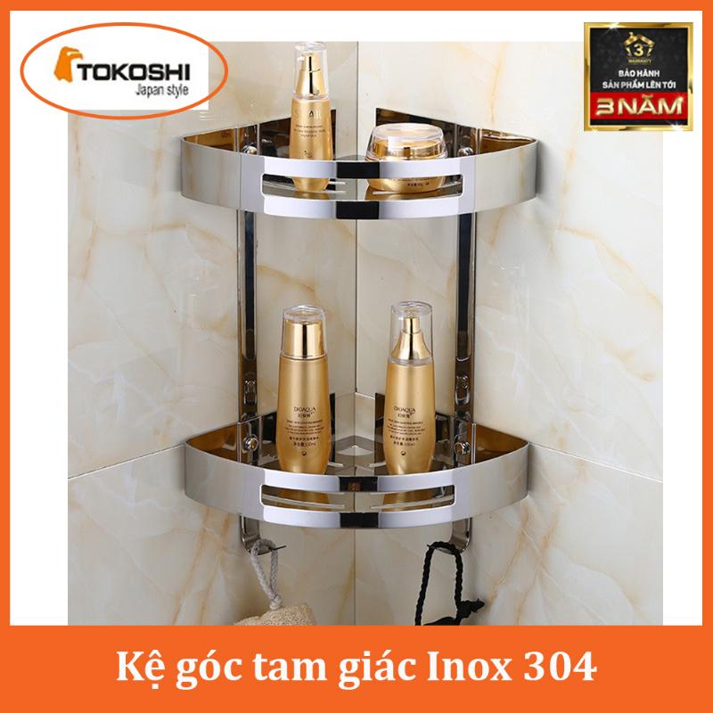 Một chiếc kệ góc nhà tắm bằng kính cường lực hoặc inox sáng bóng, thiết kế nhiều tầng, chứa các chai lọ sữa tắm, dầu gội cao cấp, được sắp xếp gọn gàng và có thêm một chậu cây xanh nhỏ, thể hiện sự sang trọng và tính ứng dụng cao.