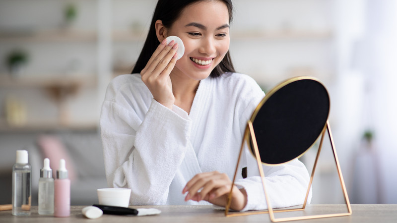 Một cô gái trẻ đang dùng bông tẩy trang thấm toner để lau nhẹ lên mặt